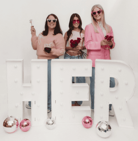 Women standing by a sign that says "her" holding flowers
